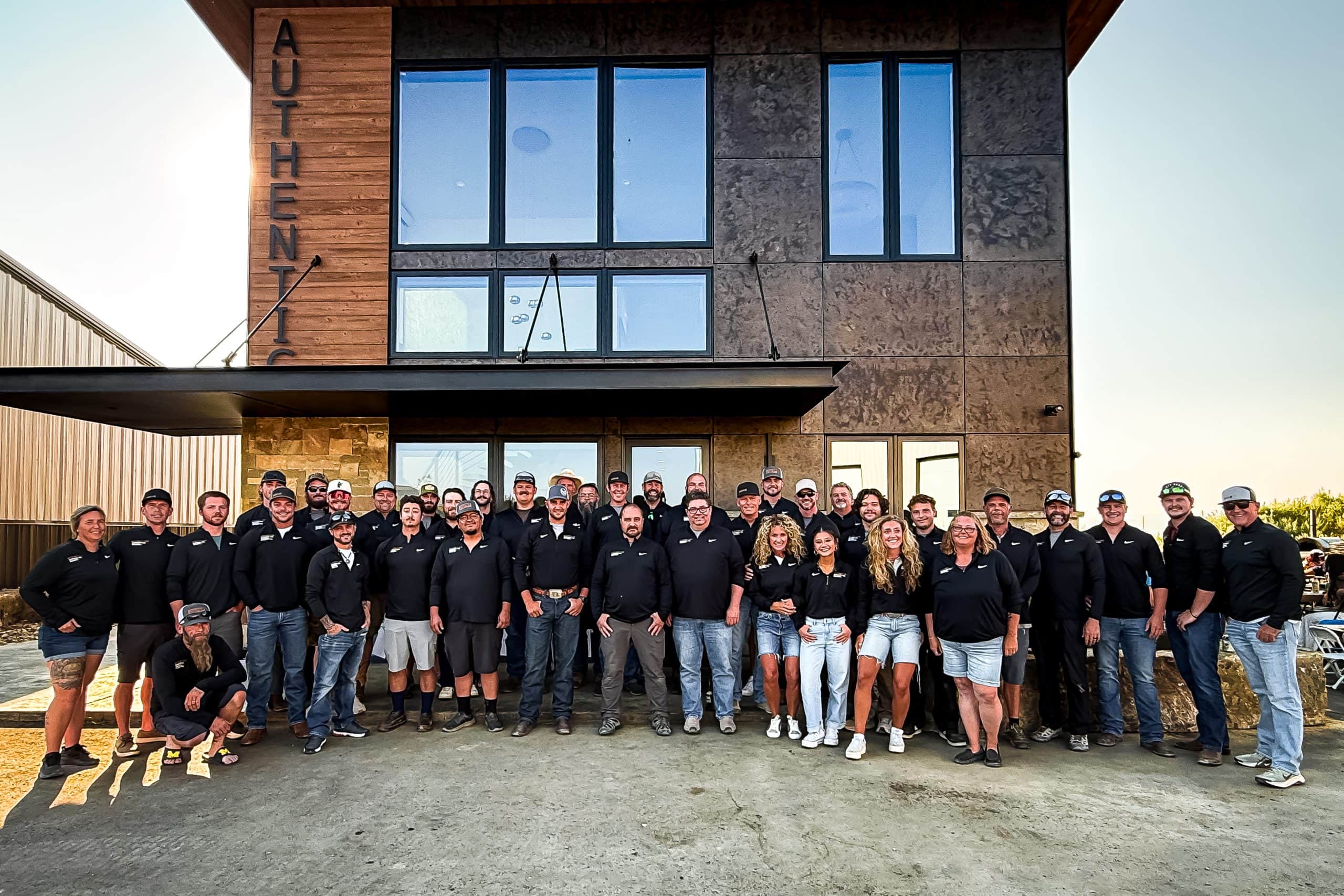 Authentic Inc. construction team gathered outside the company office in front of a wood, stone, and metal building.